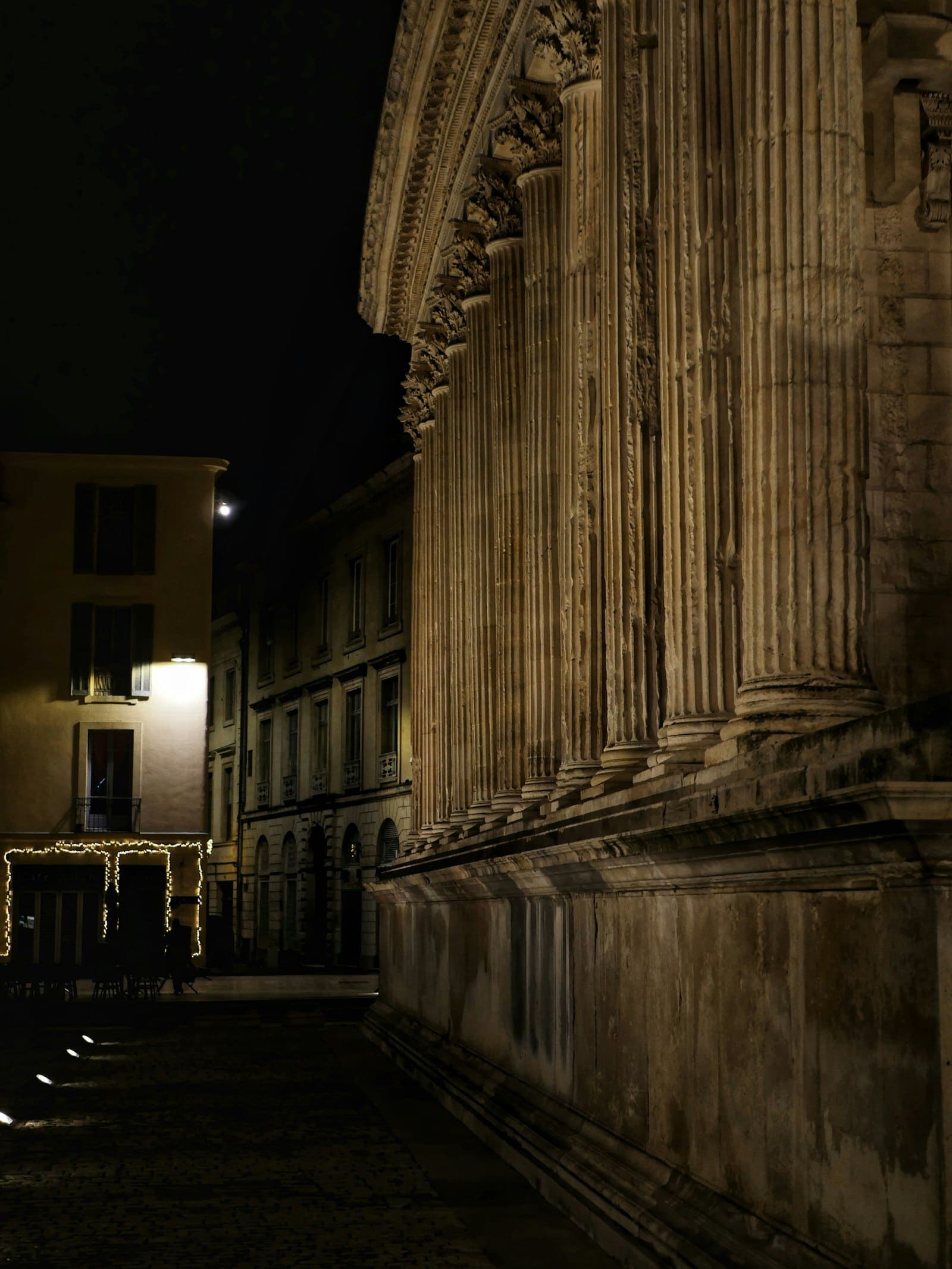 Ancient Roman columns and a temple front, lit at night.