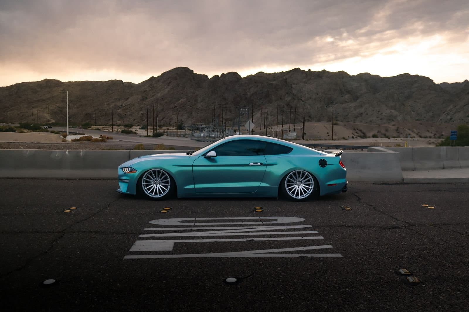 Teal sports car parked on a desert road at dusk
